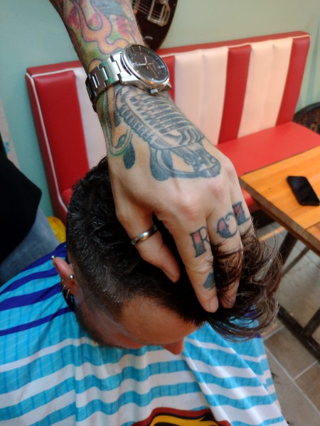 Getatoeëerde hand van Raymon op het hoofd van een klant, in het rode bankje